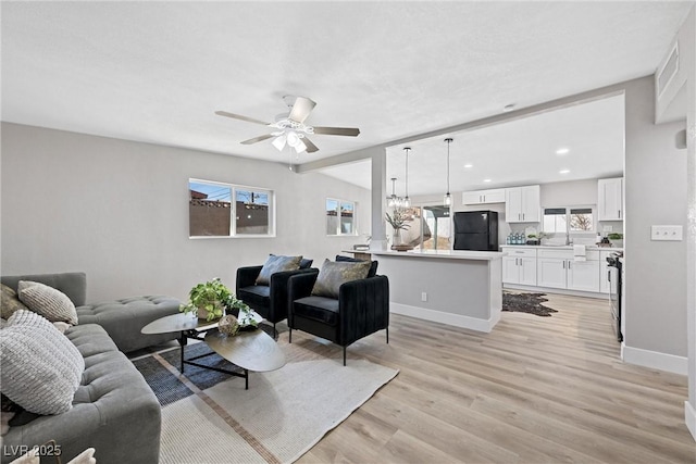 living room with ceiling fan with notable chandelier and light hardwood / wood-style floors