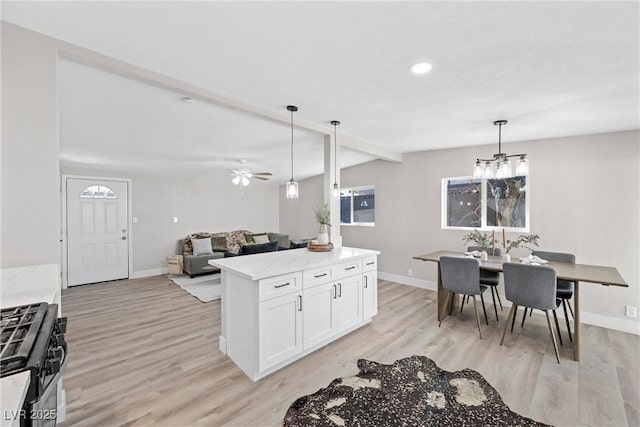 kitchen with pendant lighting, light hardwood / wood-style flooring, light stone countertops, white cabinets, and gas range