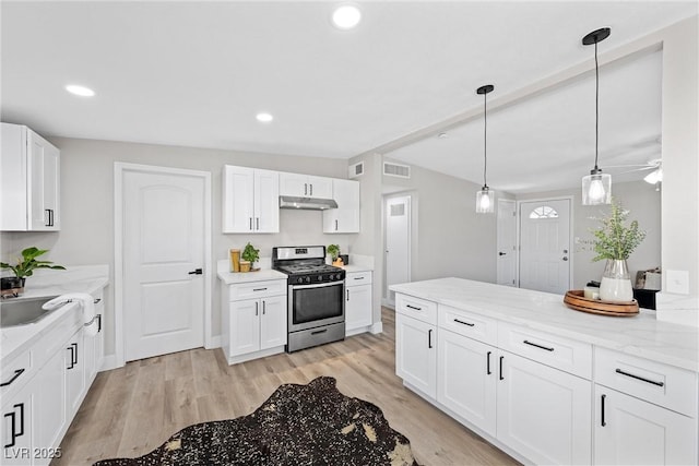 kitchen with decorative light fixtures, stainless steel gas stove, white cabinetry, light stone countertops, and light hardwood / wood-style flooring