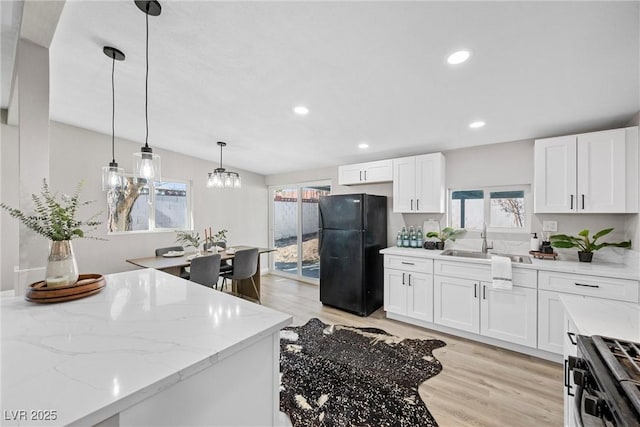 kitchen with pendant lighting, sink, stainless steel gas stove, white cabinets, and black fridge