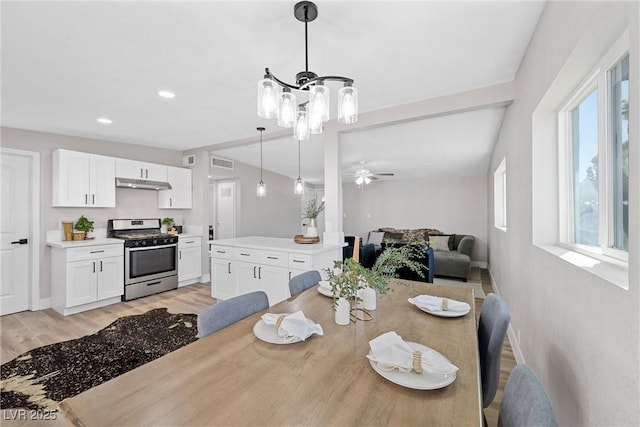 dining area featuring lofted ceiling, ceiling fan with notable chandelier, and light hardwood / wood-style flooring