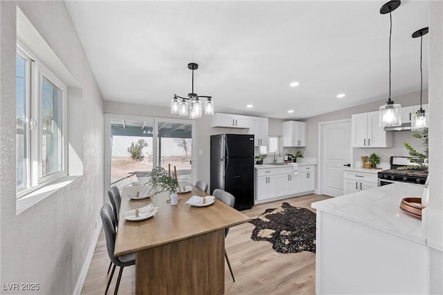 kitchen with gas range, black refrigerator, white cabinets, and light hardwood / wood-style flooring