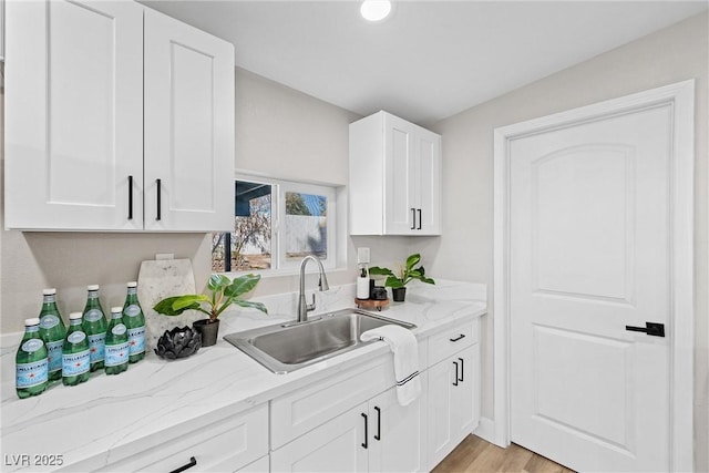 kitchen with white cabinetry, light stone countertops, sink, and light hardwood / wood-style floors