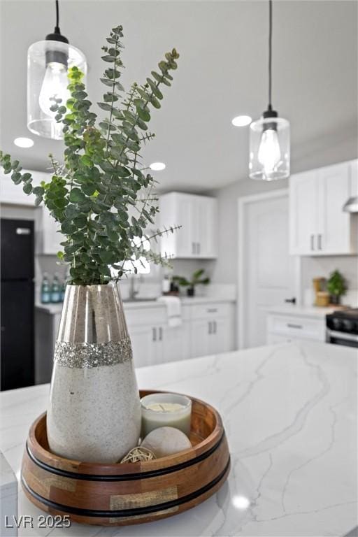 kitchen with light stone countertops, white cabinetry, black fridge, and pendant lighting