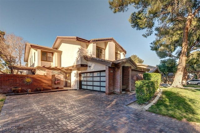 mediterranean / spanish house with a garage, brick siding, and decorative driveway