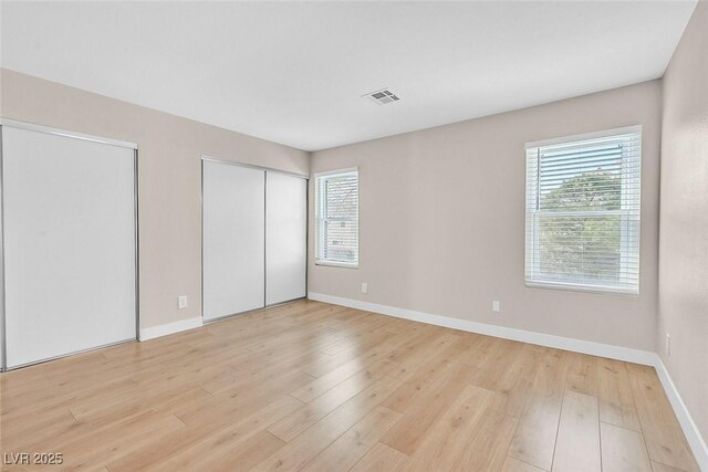 unfurnished bedroom with multiple closets, light wood-type flooring, and multiple windows