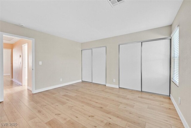 unfurnished bedroom featuring two closets and light wood-type flooring