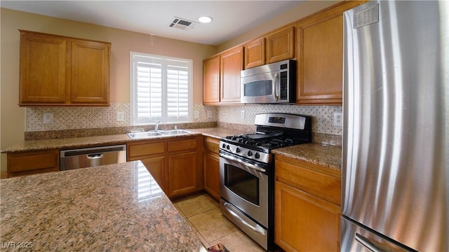 kitchen featuring stainless steel appliances, light stone countertops, sink, and light tile patterned floors