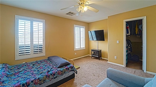 bedroom featuring a spacious closet, a wood stove, ceiling fan, and carpet flooring