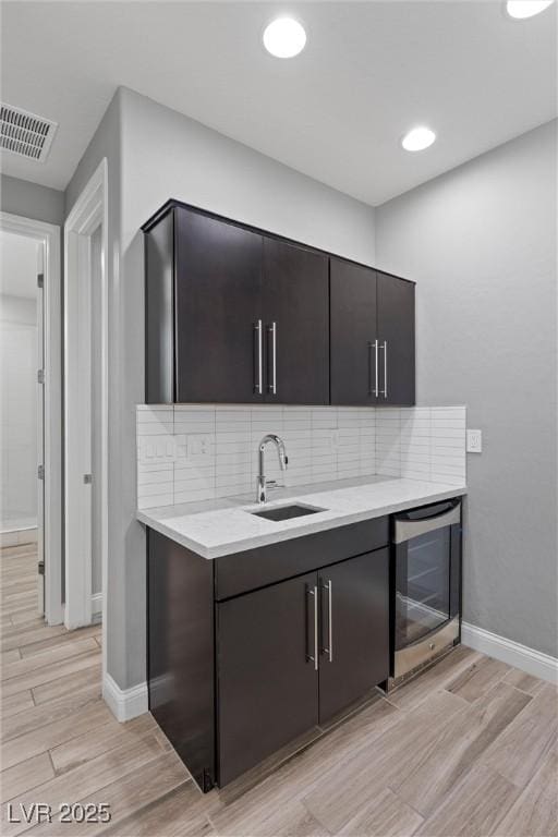 kitchen featuring wine cooler, sink, tasteful backsplash, dark brown cabinets, and light hardwood / wood-style floors