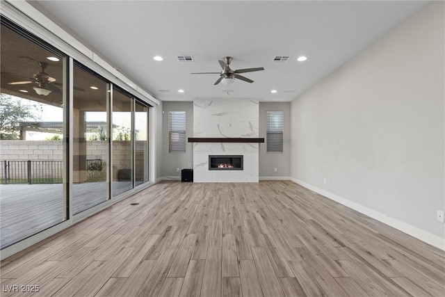 unfurnished living room with ceiling fan, a premium fireplace, and light hardwood / wood-style flooring