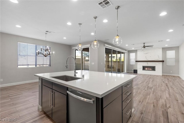 kitchen featuring sink, a large fireplace, an island with sink, stainless steel dishwasher, and light wood-type flooring