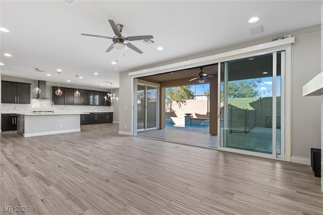 unfurnished living room featuring ceiling fan with notable chandelier and light hardwood / wood-style floors