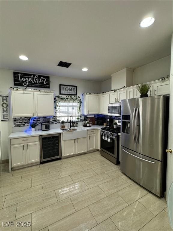 kitchen featuring sink, appliances with stainless steel finishes, white cabinetry, backsplash, and beverage cooler