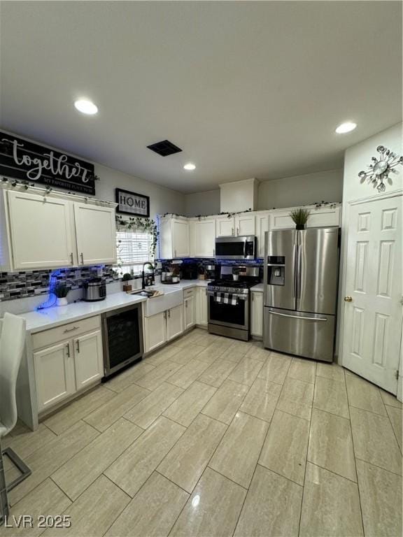 kitchen with tasteful backsplash, appliances with stainless steel finishes, wine cooler, and white cabinets