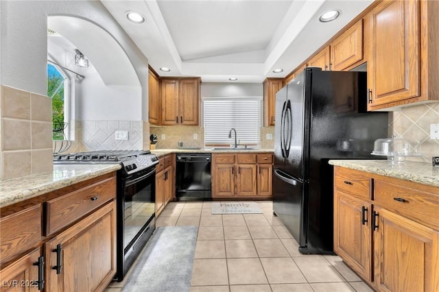 kitchen with light stone counters, light tile patterned floors, sink, and black appliances