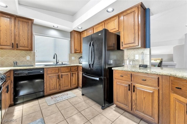 kitchen with sink, light tile patterned floors, a raised ceiling, light stone countertops, and black appliances