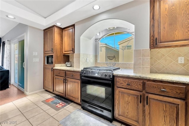 kitchen with backsplash, light tile patterned floors, light stone counters, black appliances, and a healthy amount of sunlight