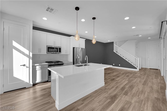 kitchen featuring sink, decorative light fixtures, a center island with sink, light hardwood / wood-style flooring, and stainless steel appliances