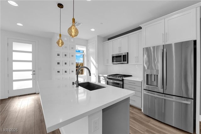 kitchen with sink, white cabinetry, hanging light fixtures, stainless steel appliances, and an island with sink