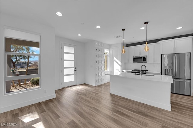 kitchen with sink, appliances with stainless steel finishes, an island with sink, pendant lighting, and white cabinets