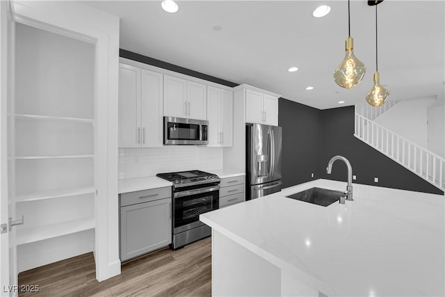 kitchen with appliances with stainless steel finishes, white cabinetry, sink, hanging light fixtures, and light hardwood / wood-style flooring