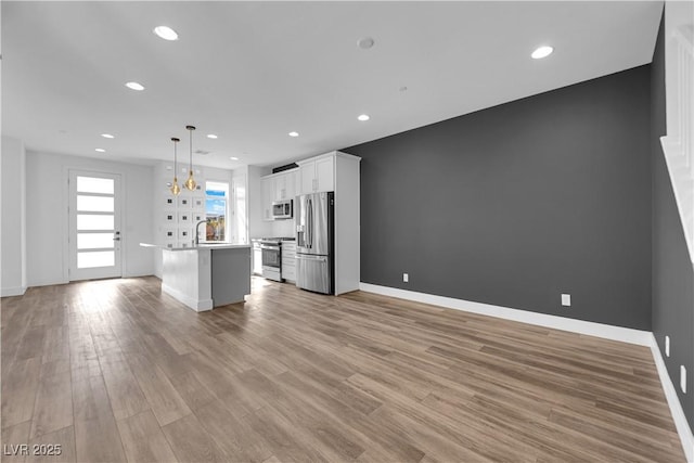 kitchen featuring hanging light fixtures, stainless steel appliances, white cabinets, a kitchen island, and light wood-type flooring