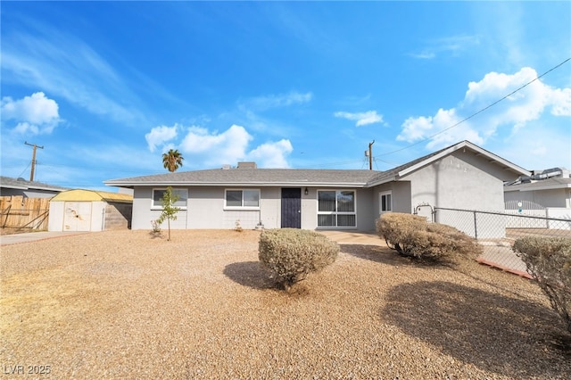 single story home featuring a storage unit, fence, an outbuilding, and stucco siding