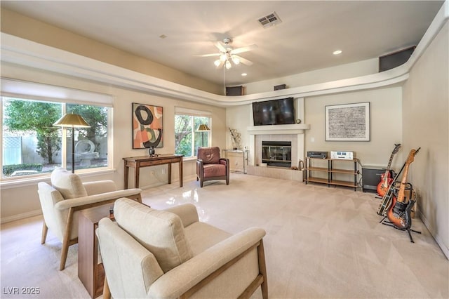 living room featuring a fireplace, light colored carpet, and ceiling fan