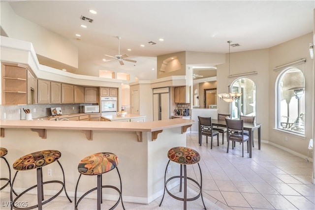 kitchen featuring ceiling fan with notable chandelier, a breakfast bar area, backsplash, light tile patterned floors, and paneled built in fridge