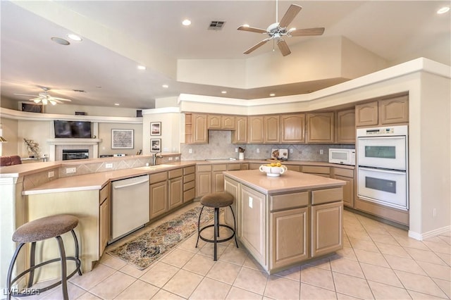 kitchen with white appliances, a breakfast bar, backsplash, a center island, and light tile patterned flooring