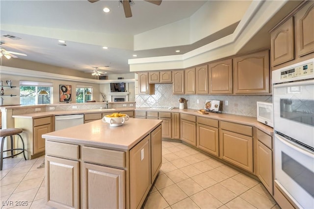 kitchen with white appliances, a center island, tasteful backsplash, kitchen peninsula, and light brown cabinets