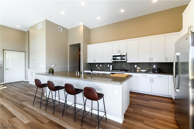 kitchen with a kitchen bar, sink, white cabinetry, appliances with stainless steel finishes, and a kitchen island with sink