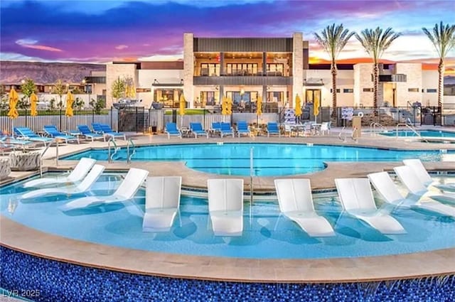 pool at dusk with a hot tub and a patio