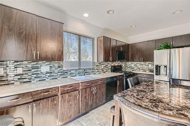 kitchen with black appliances, sink, decorative backsplash, light stone counters, and dark brown cabinetry