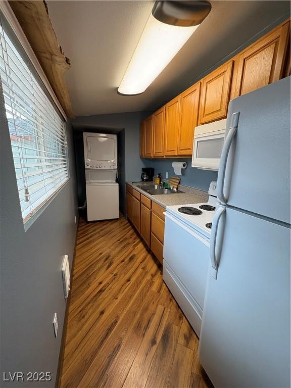 kitchen featuring stacked washer and dryer, wood-type flooring, sink, and white appliances