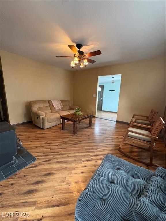 living room with ceiling fan, a wood stove, and light hardwood / wood-style floors