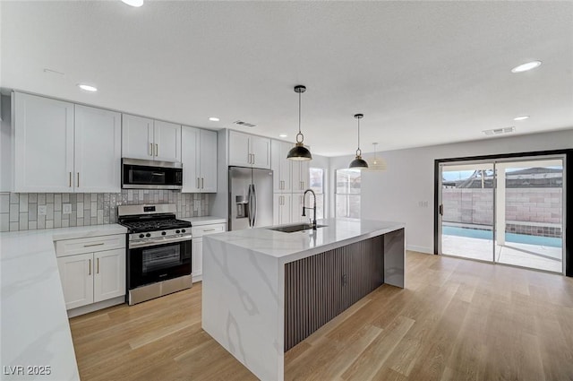 kitchen with sink, appliances with stainless steel finishes, hanging light fixtures, white cabinets, and a center island with sink