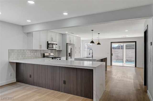 kitchen featuring white cabinetry, hanging light fixtures, kitchen peninsula, and appliances with stainless steel finishes