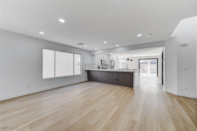 kitchen with appliances with stainless steel finishes, decorative light fixtures, sink, kitchen peninsula, and light hardwood / wood-style flooring