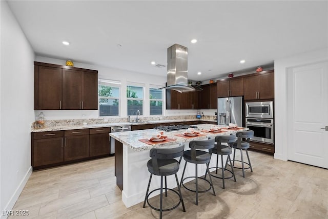 kitchen featuring sink, a breakfast bar area, appliances with stainless steel finishes, island range hood, and a kitchen island