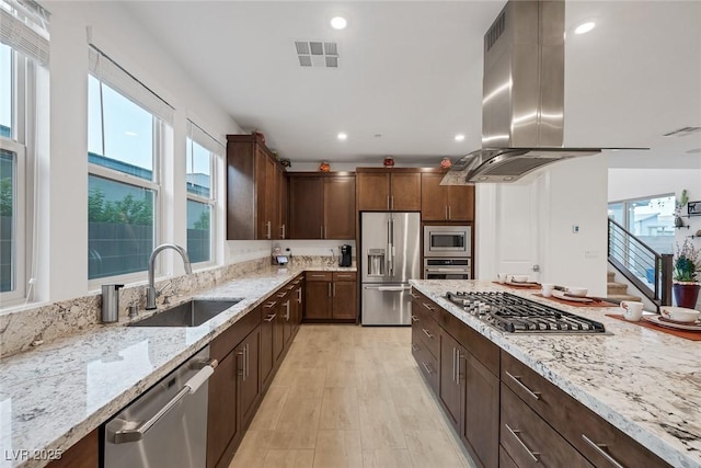 kitchen featuring sink, dark brown cabinets, stainless steel appliances, island range hood, and light stone countertops