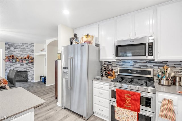 kitchen featuring appliances with stainless steel finishes, a fireplace, decorative backsplash, and white cabinets