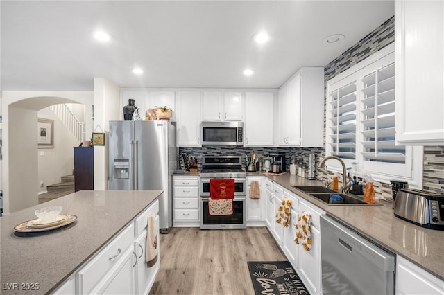 kitchen featuring sink, backsplash, stainless steel appliances, light stone counters, and white cabinets