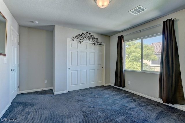 unfurnished bedroom featuring dark colored carpet and a textured ceiling