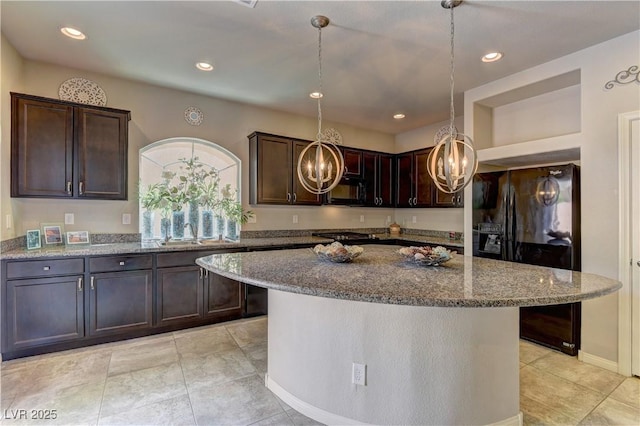 kitchen with light stone countertops, decorative light fixtures, black appliances, and a center island