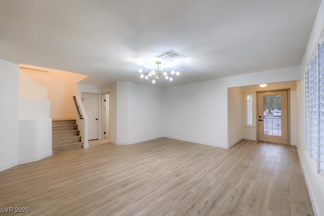 unfurnished room featuring an inviting chandelier, visible vents, stairway, and light wood finished floors