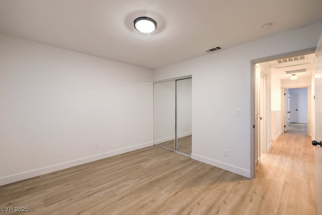 unfurnished bedroom with light wood finished floors, baseboards, visible vents, and a closet