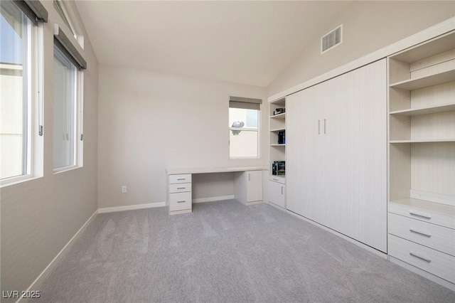 unfurnished office featuring light colored carpet, lofted ceiling, and built in desk