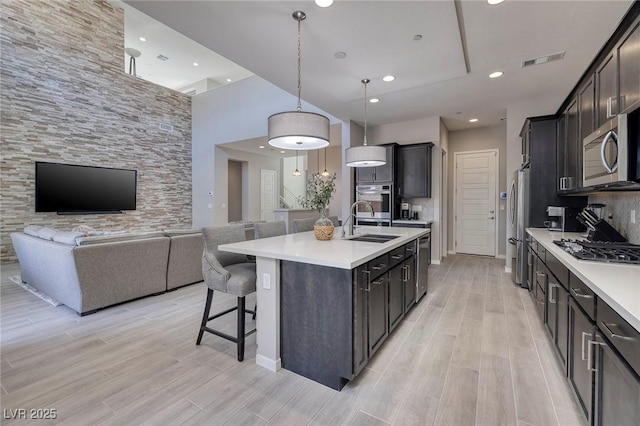 kitchen with appliances with stainless steel finishes, a breakfast bar, pendant lighting, sink, and a kitchen island with sink